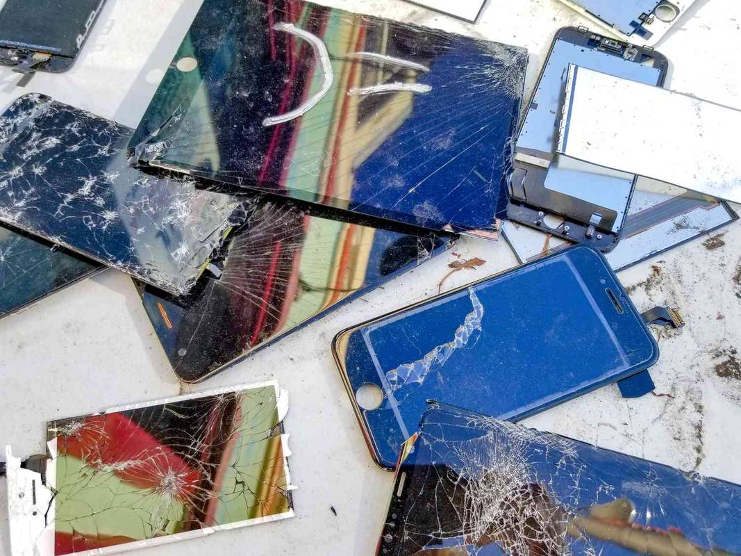 Beberapa smartphone dan tablet rusak dengan layar retak di atas meja.