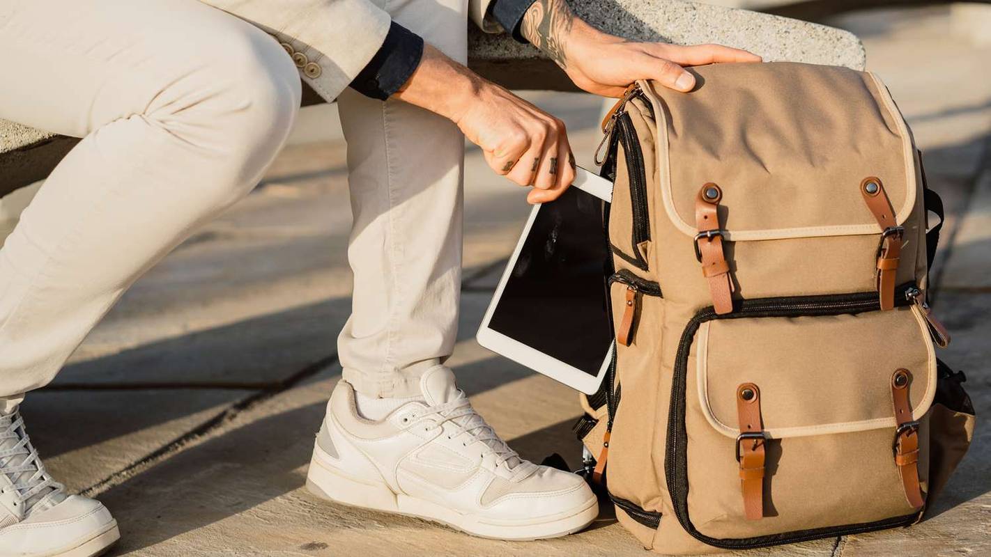 Muž v bílých kalhotách vkládá svůj iPad do batohu.