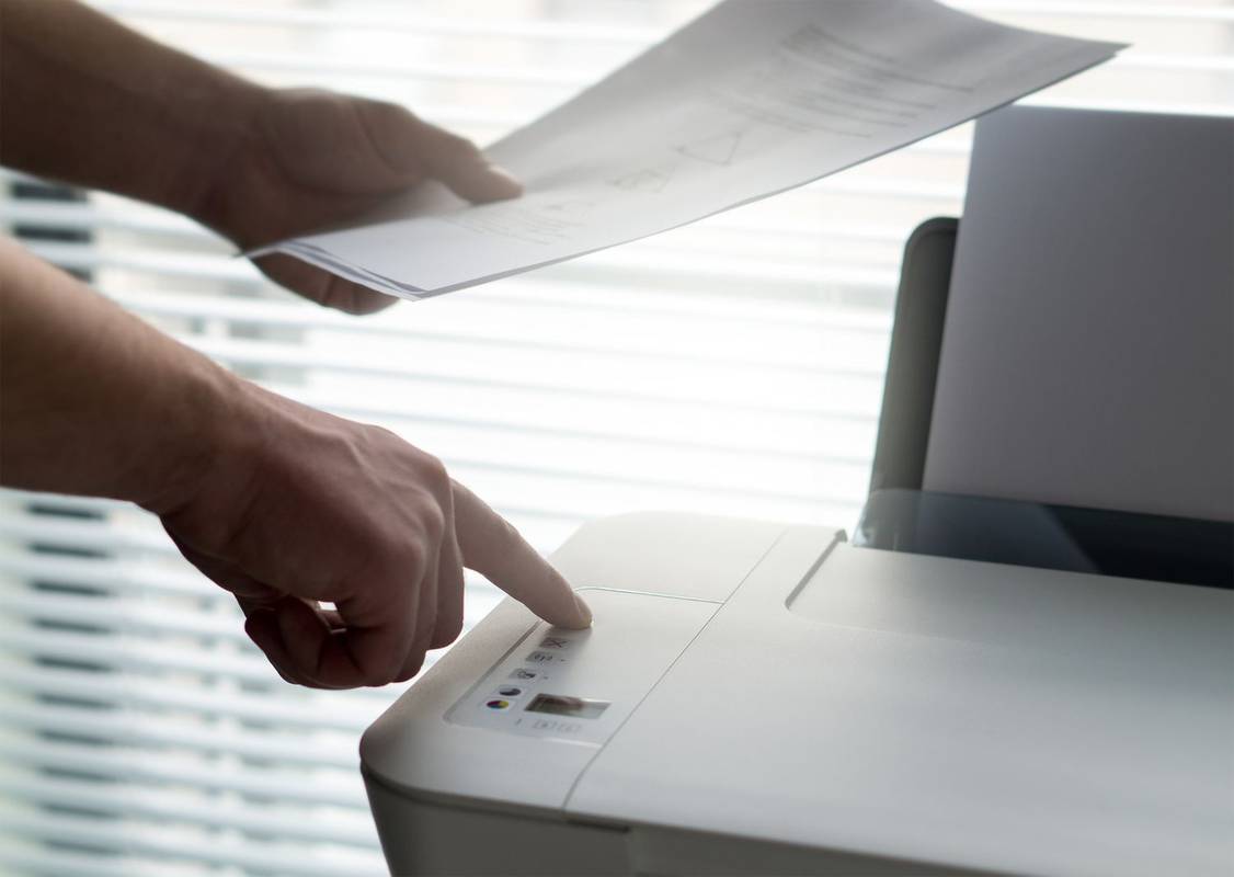 Ktoś trzyma papiery i naciska przycisk na drukarce, aby zatrzymać zadanie drukowania