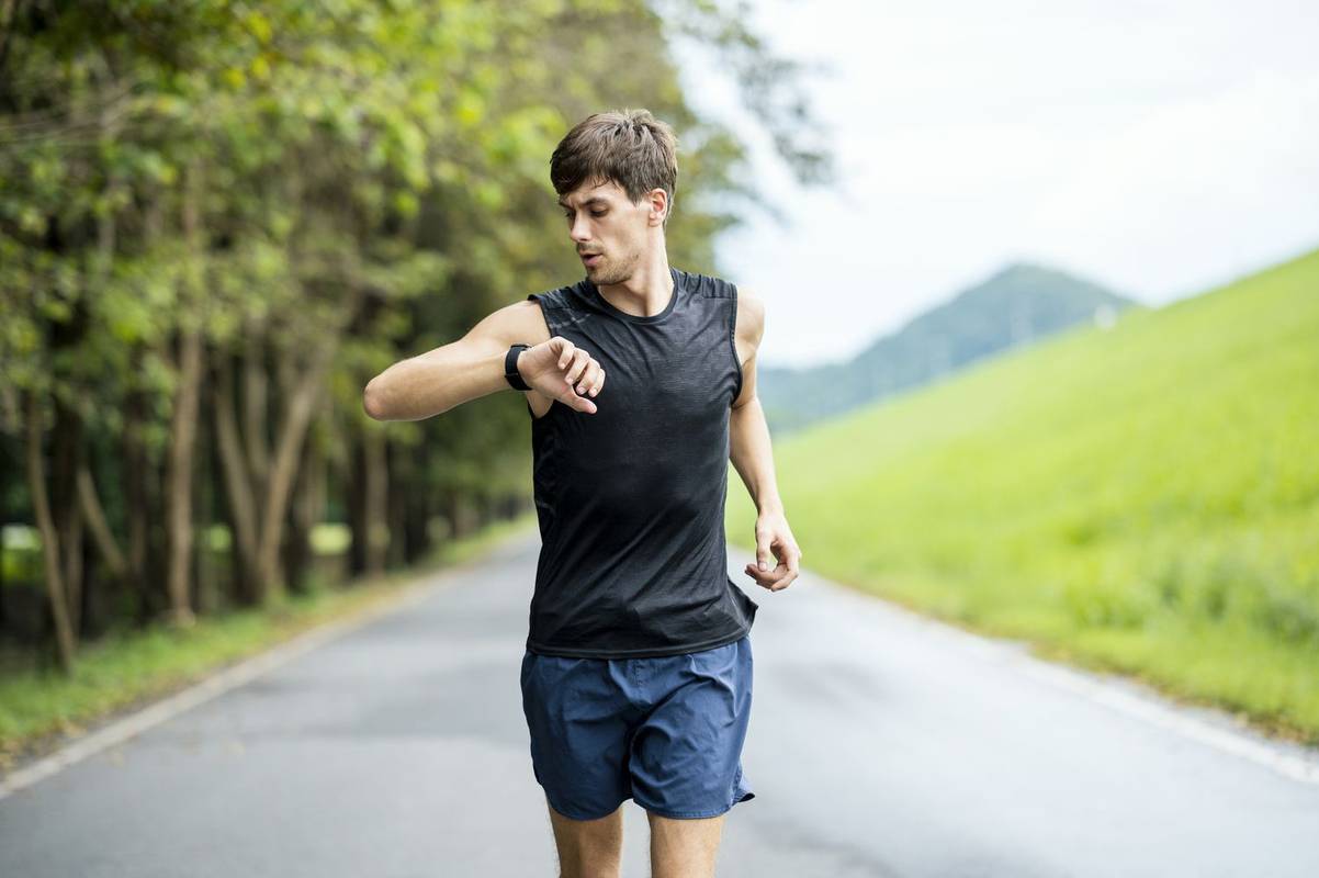 Běžec běží na přírodní stezce a dívá se na svůj smartphone