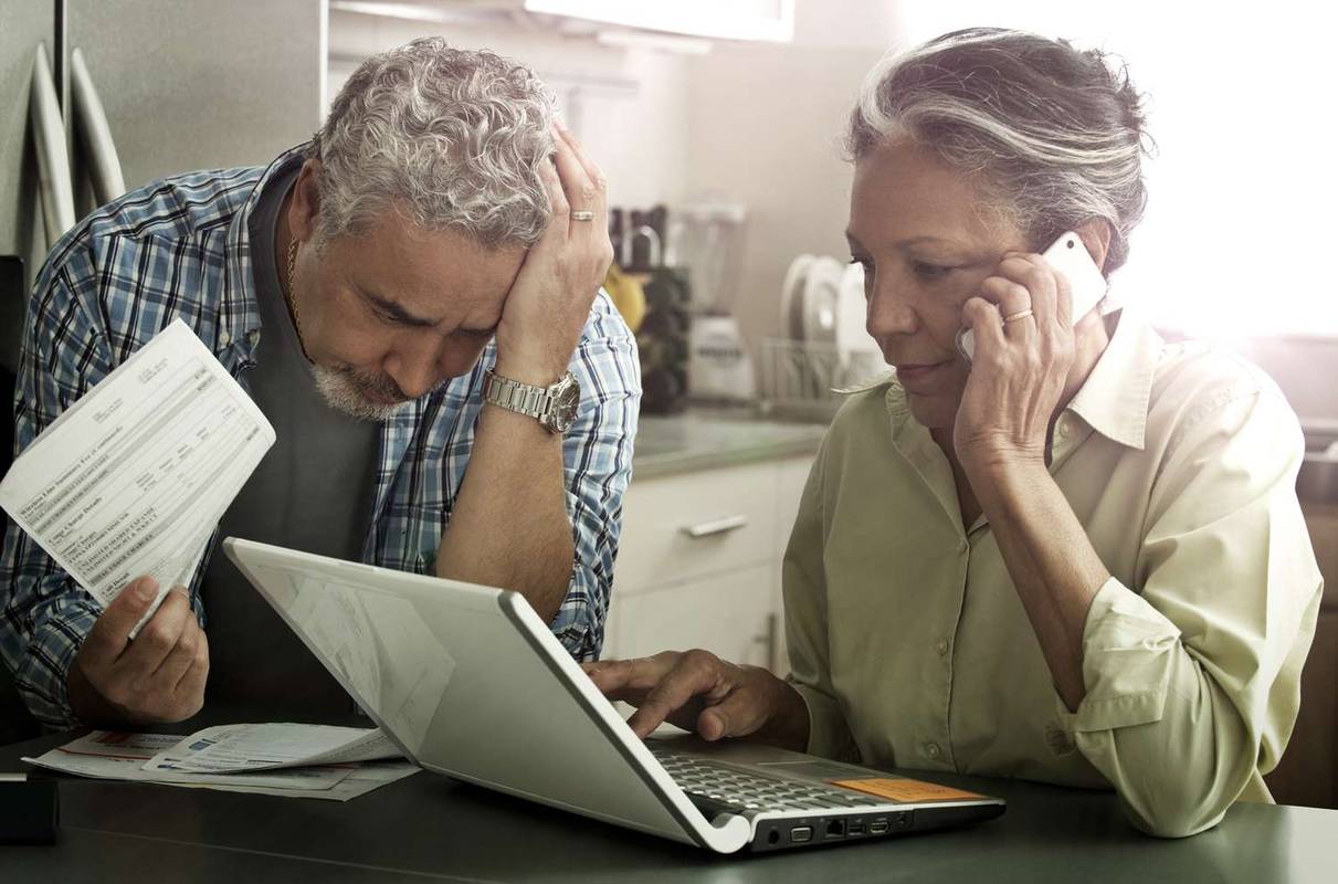 Bejaard echtpaar met een laptop, mobiele telefoon en telefoonrekeningen.